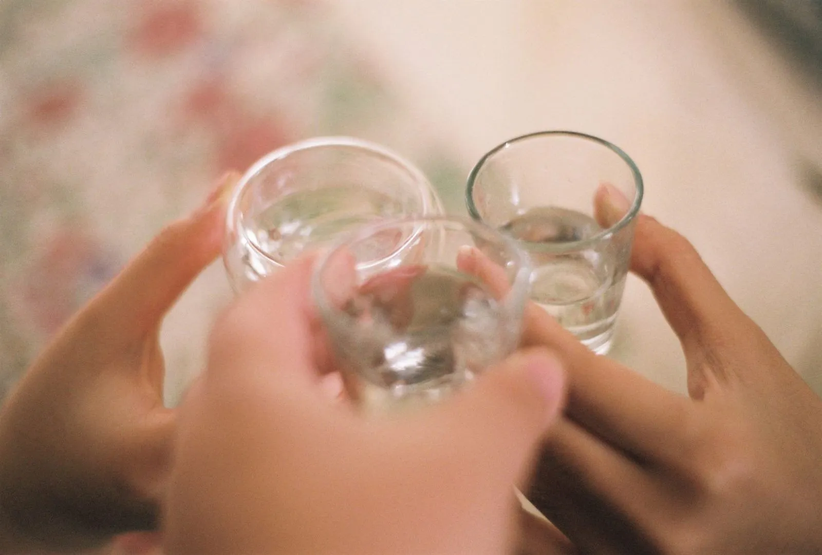 Brindis con vasitos de soju: tres manos chocando vasos de shot de vidrio