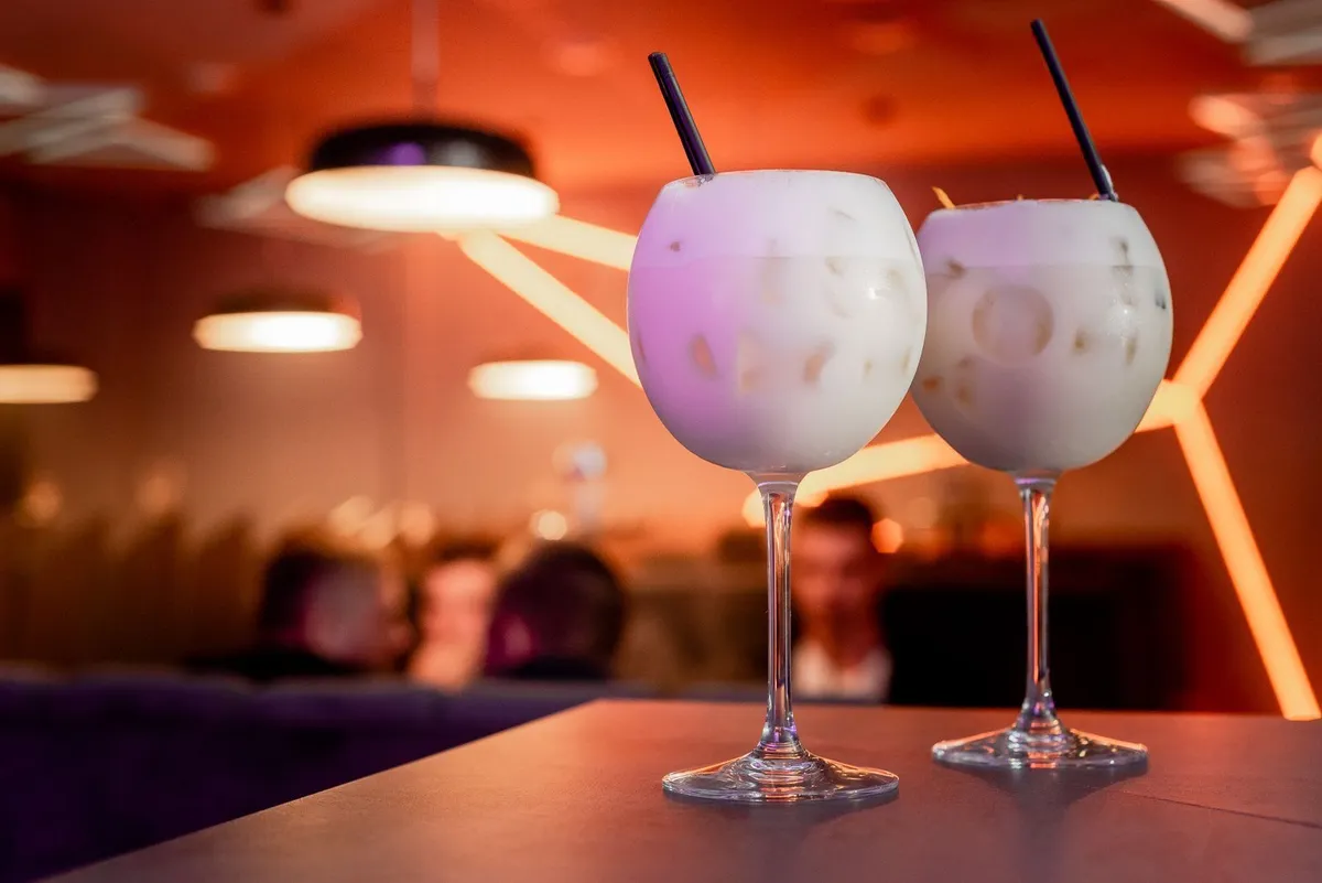 Dos copas con un trago blanco y cremoso con hielo y sorbete negro sobre la barra de un bar